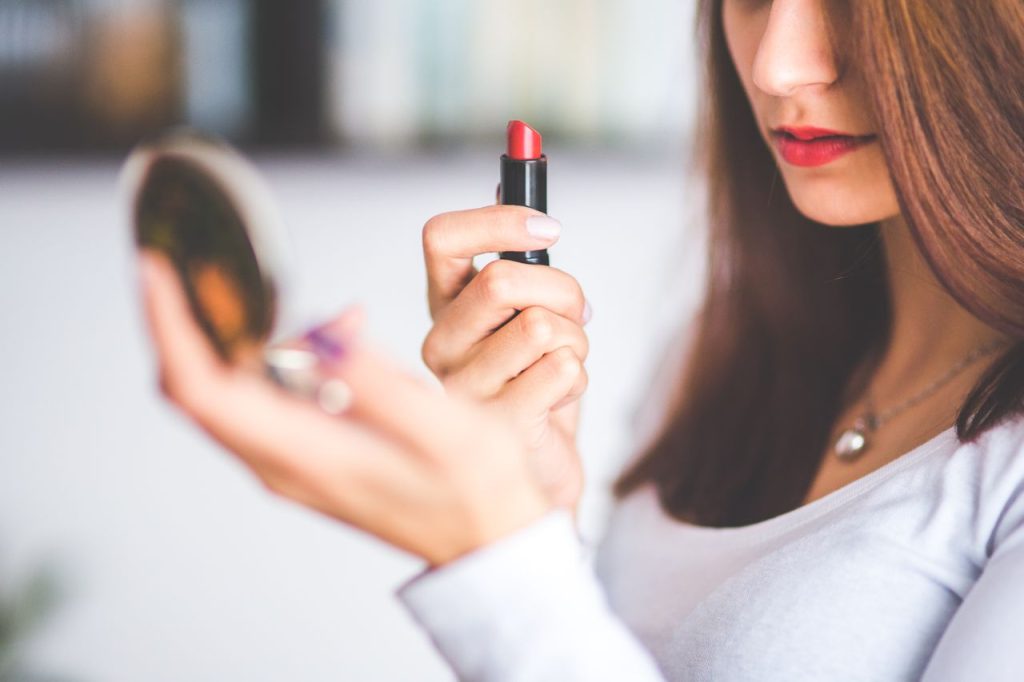 Woman applying lipstick while using a compact mirror