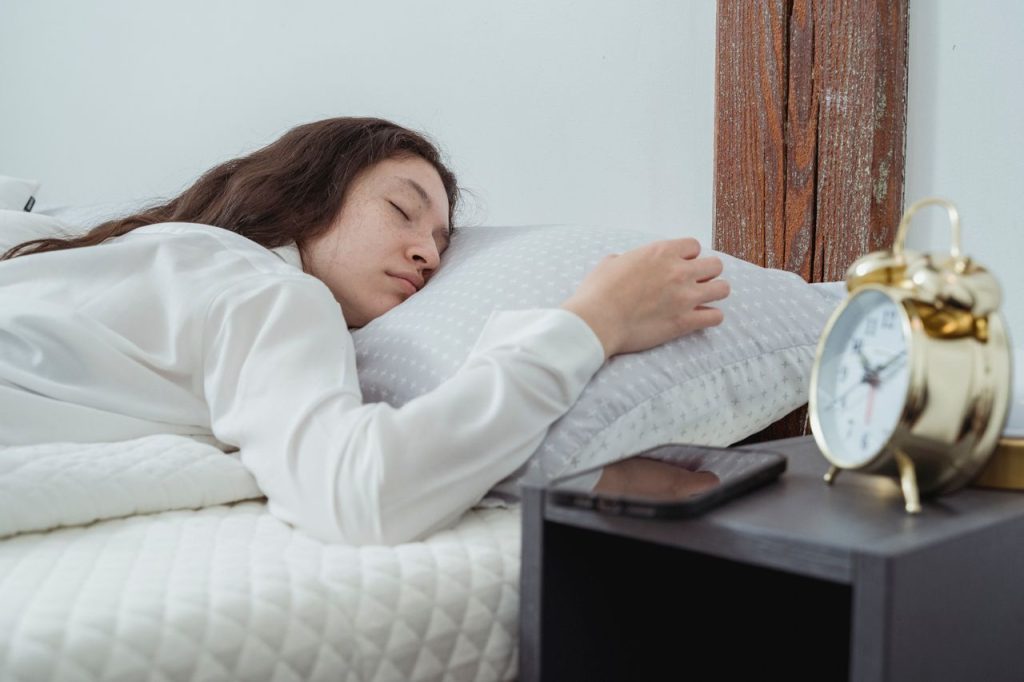 Woman sleeping peacefully in a comfortable bedroom with a smartphone and alarm clock nearby