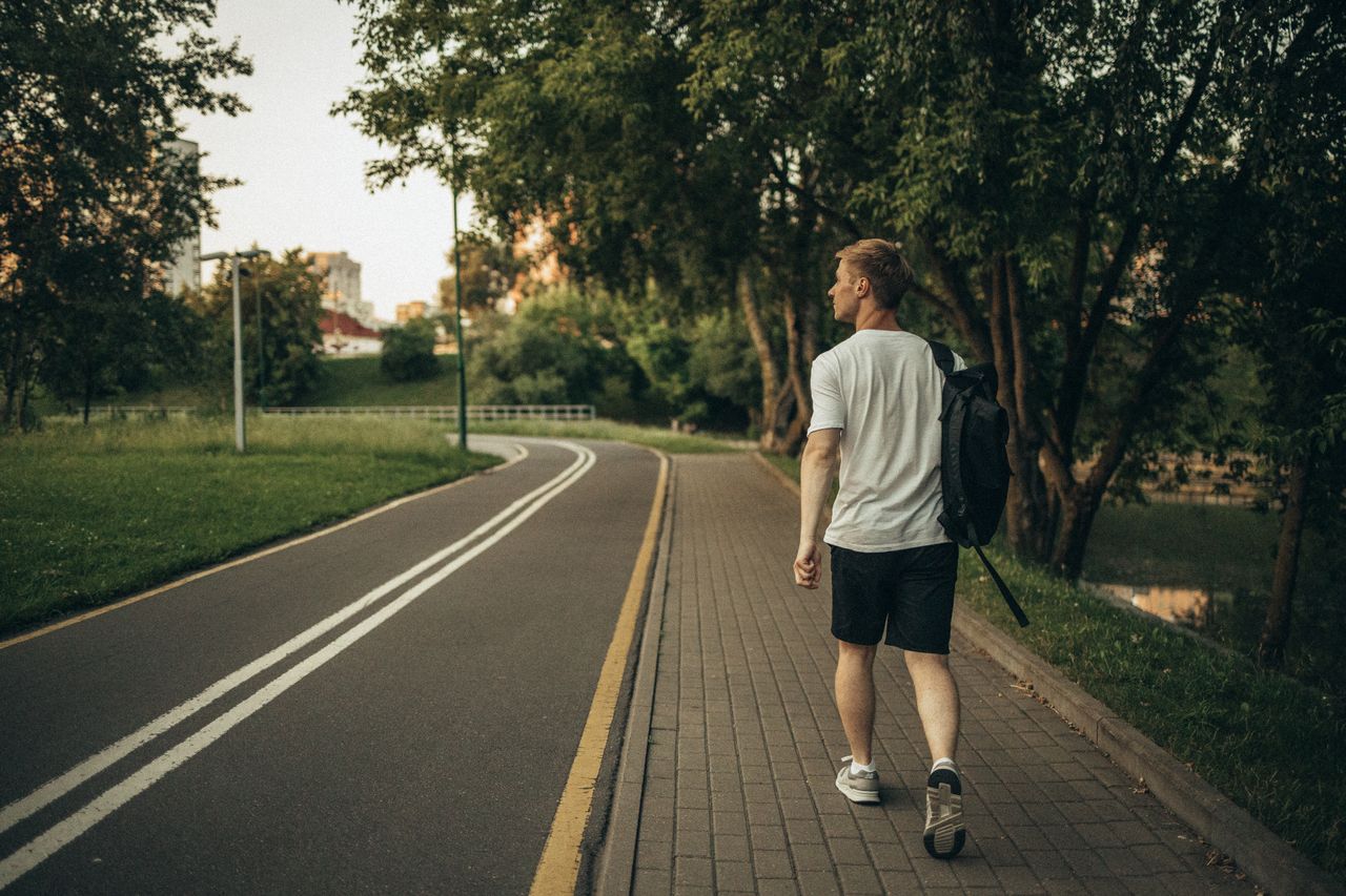 A man walking along a peaceful, tree-lined park path.